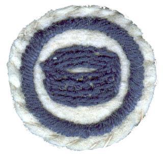 Picture of round white felt badge with a logo of a round woven basket embroidered in dark blue thread, surrounded by a ring of dark blue stitching.