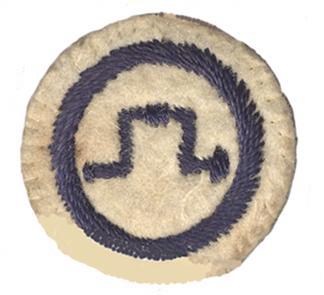 Photo of round white felt badge with image of a brace drill stitched in dark blue thread within a dark blue stitched ring.