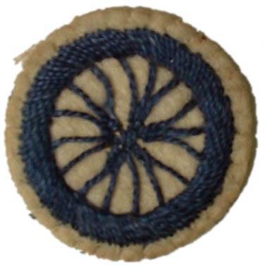 Image of round white felt badge with a logo of a bicycle wheel embroidered in navy thread.