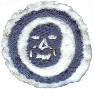 Image of round white felt badge with logo of mask in navy stitching with white detailing, set in a navy embroidered ring.