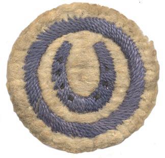image of round white felt badge with horseshoe logo embroidered in dark blue thread, within a dark blue embroidered ring