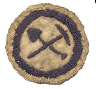Image of round white felt badge with logo of crossed shovel and pick embroidered in navy thread, in a navy embroidered ring.