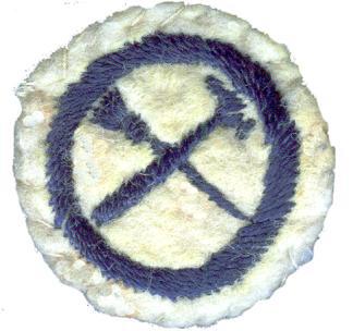 Image of round white felt badge with logo of crossed hammer and paint brush embroidered in navy within a navy embroidered ring.