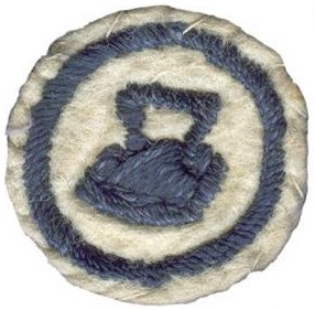 Image of round white felt badge with embroidered flat iron logo in navy thread, within an embroidered navy ring.