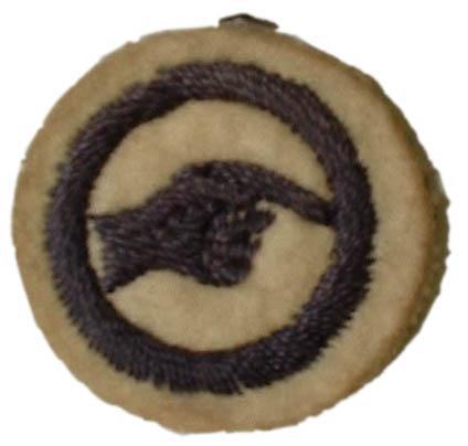 Image of round white felt badge with logo of hand pointing right embroidered in navy thread within a navy embroidered ring