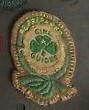 Image of Green First Class Badge, featuring a Second Class Badge with green trefoil and lettering on a beige woven badge, sewn onto the centre of a larger beige woven badge, with a green knotted scroll which surrounds the second class badge, with yellow "Be Prepared" lettering on the green scroll