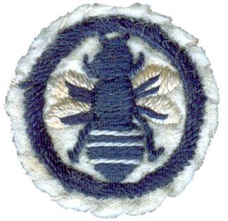 Photo of round white felt badge with logo of a bee in dark blue stitching with white highlights, within an embroidered dark blue ring.