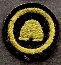 Guide Bee Farmer badge image, showing a domed beehive stitched in green within a green stitched ring, on a black felt background