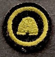 Image of Guide Bee Farmer badge with a logo of a domed beehive in a ring, all embroidered in green on black felt