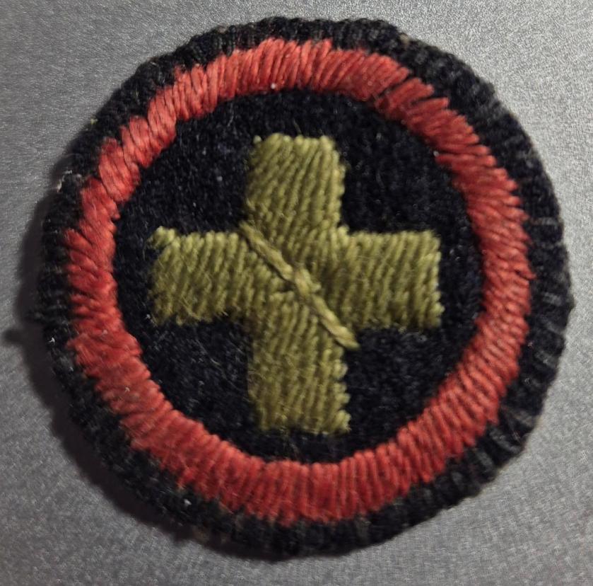 Black felt badge featuring an embroidered green cross within a red embroidered ring.